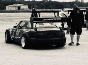 Man standing next to Miata race car with AMP EFI logo on wing